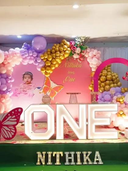 A grand butterfly themed first birthday stage. This impressive setup features large light-up letters spelling "ONE", a personalized backdrop, and a lush balloon arrangement in pink, purple, and gold.