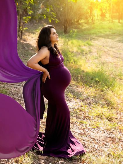 A powerful and dramatic outdoor portrait. The flowing purple fabric of the gown catches the wind, creating a stunning silhouette against the golden sunlight.