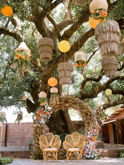 The unique and rustic decor for a Haldi ceremony, with jute chandeliers and floral arrangements hanging from a large tree.