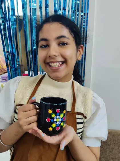 A bright smile from a guest holding her finished dot mandala mug, a result of a fun and creative birthday activity.