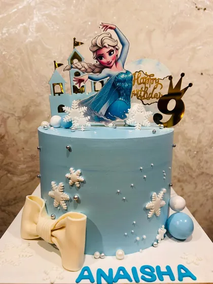A lovely light blue Frozen cake for a 9th birthday, decorated with an Elsa figurine, snowflakes, and a fondant bow.