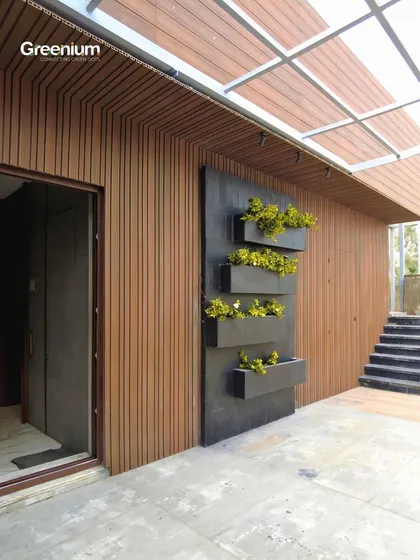 This terrace wall in Pitampura was enhanced with warm wooden paneling and a modern black planter rack. The contrast between the wood and the yellow flowers creates a striking and stylish feature.