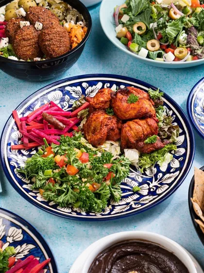 A vibrant spread of Middle Eastern food, featuring chicken shish tawook on a beautiful blue patterned plate. The colorful salads and dips surrounding it create a feeling of a generous, flavorful feast.