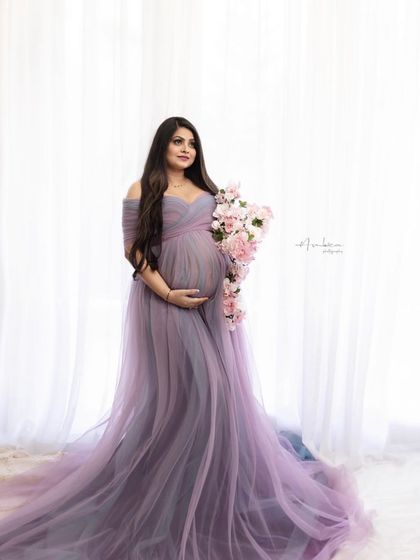 A vision in lavender. This beautiful off-the-shoulder tulle gown, accessorized with a bouquet of pink flowers, creates a soft, romantic, and utterly timeless maternity portrait.