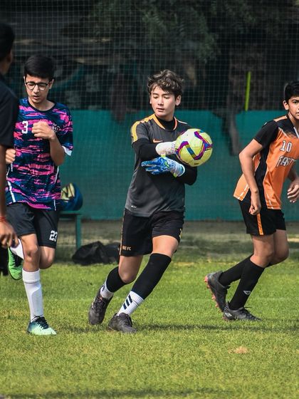 A goalkeeper confidently catches the ball, securing it for his team during a match.
