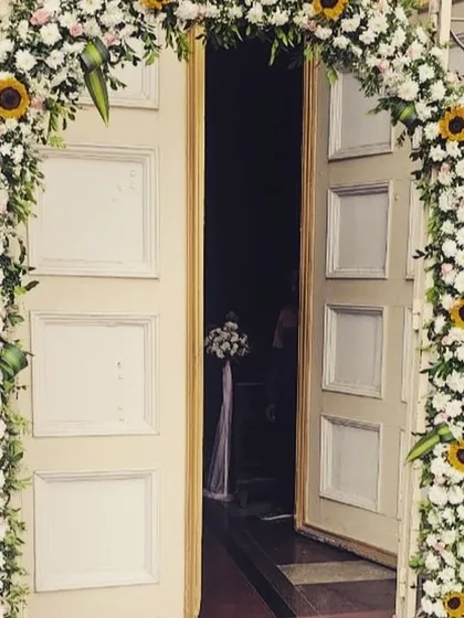 A classic and cheerful floral archway for a church wedding entrance. The arch is covered in white chrysanthemums and bright yellow sunflowers, creating a welcoming and joyous first impression.