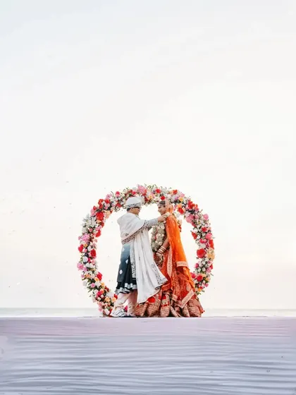 A stunning shot of the couple framed by a circular floral mandap against the backdrop of the ocean.