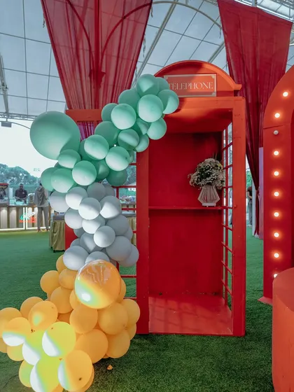 Even classic props get a whimsical twist. A traditional red telephone booth is transformed with a cascade of colorful balloons, serving as a unique photo spot within the vibrant carnival theme.