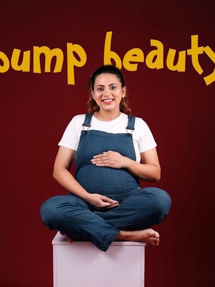 Titled 'Bump Beauty', this portrait celebrates the beauty of the pregnant form in a fun, casual way. The mother-to-be sits cross-legged, smiling warmly in her overalls.