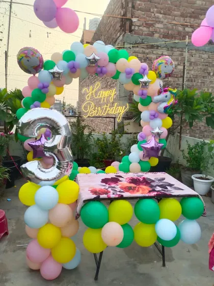 A unicorn-themed 3rd birthday setup on a rooftop. The pastel-colored balloon arch around the cake table looks beautiful in an outdoor setting.