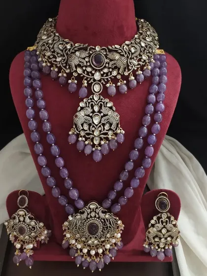 A layered Victorian jewelry set in a lovely lavender hue. The set includes a choker, a short necklace, and a long beaded necklace with matching earrings, all featuring intricate peacock motifs.
