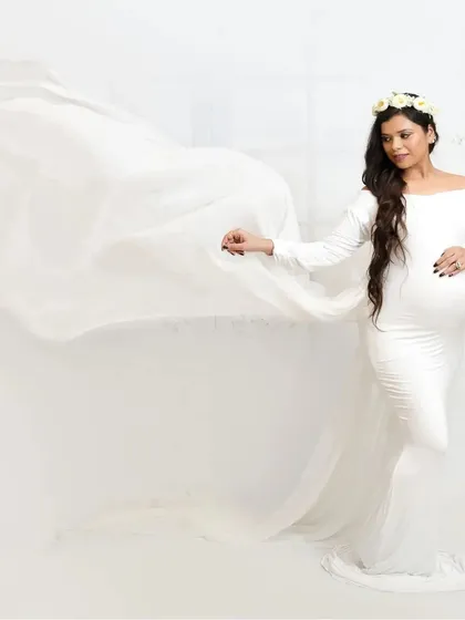 This portrait showcases the beautiful silhouette of pregnancy. The mother-to-be, dressed in a form-fitting white gown with a flowing train, looks off to the side, creating an elegant and contemplative image.