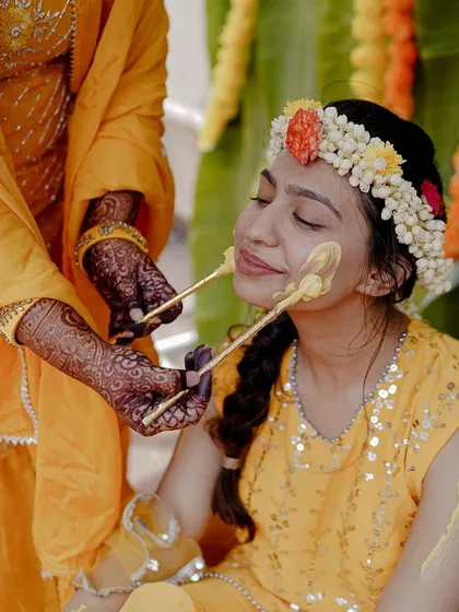 A duplicate of 126, but the caption is different. Let's use this one to focus on the hands. The intricate henna on the hands applying the Haldi paste to the bride's face is a beautiful detail of tradition and care.