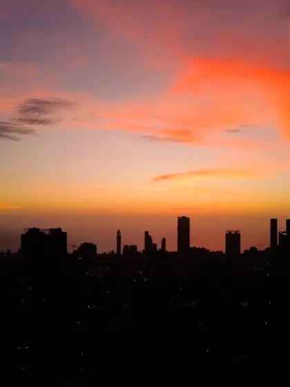 A large, dramatic orange cloud hovers over the silhouetted Mumbai skyline at dusk.