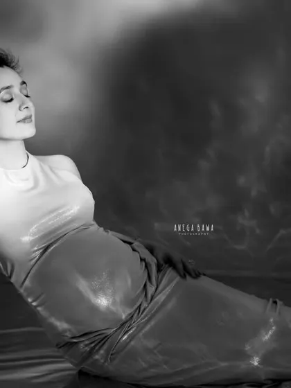 A dramatic, artistic portrait with a unique backdrop. In black and white, the textures of the background and reflective floor become even more pronounced.