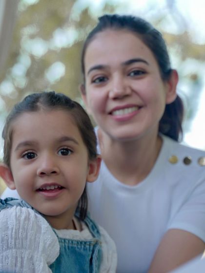 A close-up portrait of a mother and daughter, highlighting their happy expressions in a bright, outdoor setting.