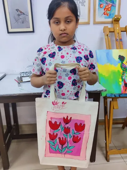 A young girl proudly holds up the tote bag she painted herself in one of our creative workshops.
