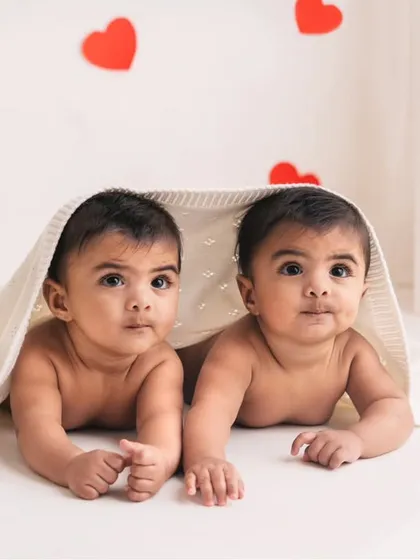 Peek-a-boo! These curious twins are looking out from under a blanket, their big, bright eyes full of wonder.