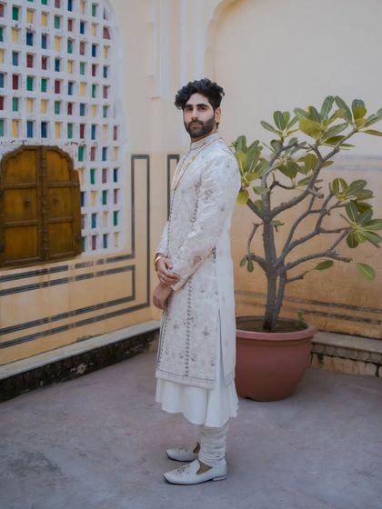 A full-length groom portrait, showcasing his elegant white sherwani against a backdrop of colorful stained glass.