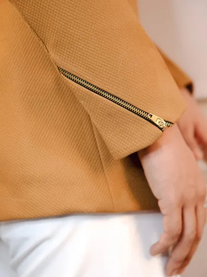 A close-up on the sleeve of the tan bandhgala, highlighting the quality of the fabric and the functional zipper detail on the cuff.