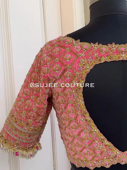 The back view of a heavily embroidered pink bridal blouse. The design features a large keyhole cutout, with every inch covered in a jaal pattern of zardozi and pearl work.