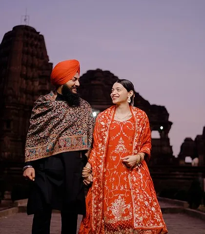Holding hands and sharing a smile, Preet and Gurleen walk through the grounds of a historic temple at dusk. This photo captures a happy, candid moment in a stunning, atmospheric setting.