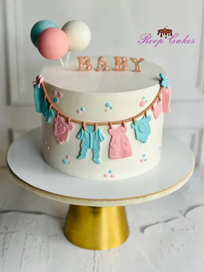 An adorable baby shower cake with a clothesline of tiny fondant outfits, perfect for welcoming a new baby.