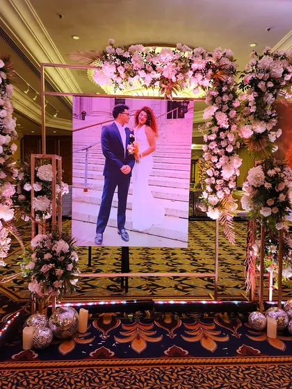 We create personalized walkways that tell your story. This entrance gallery features large, beautifully lit portraits of the couple, framed by elegant floral arrangements, allowing guests to walk through their journey of love.