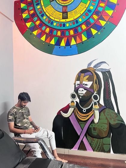 The finished mural in the tattoo studio, with a client sitting in the chair. The art serves as an inspiring backdrop for the creative work done in the space.
