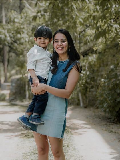 A mother holds her son in her arms, both smiling, during a walk through a park.