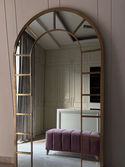 The reflection in the stunning gold-framed arched mirror reveals the full scale of the walk-in closet, including the plush purple ottoman.