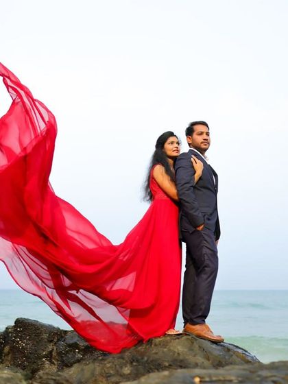 A classic pre-wedding pose on the rocks by the sea. The flowing red trail of the gown adds a dramatic and colorful touch.