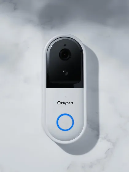A simple, top-down shot of the Phynart smart doorbell. The white marble background gives it a clean, modern, and premium feel, while the glowing blue button draws the eye.