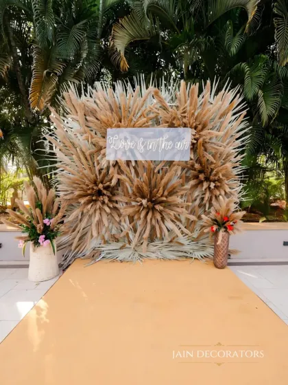 A photo booth backdrop that is pure rustic chic. A wall of pampas grass creates a soft, textured background for the "Love is in the air" sign, perfect for a modern, bohemian-themed event.