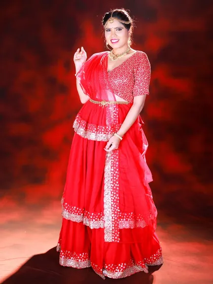 A full-length studio portrait against a dramatic red background. The lighting highlights the sequin work on the blouse and the tiered layers of the skirt.