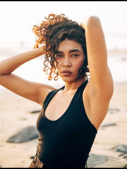 This outdoor beach portrait focuses on the model's natural beauty and curly hair texture. The soft, diffused light of the late afternoon is flattering and gentle, creating a relaxed and effortless vibe.