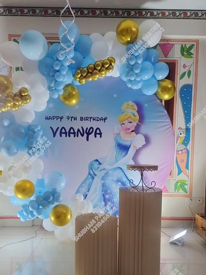 A beautiful Cinderella themed birthday decoration with a character backdrop and a blue, white, and gold balloon arrangement.