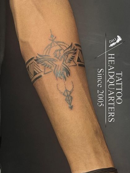 A custom armband tattoo that combines geometric patterns with a phoenix or bird symbol in the center.