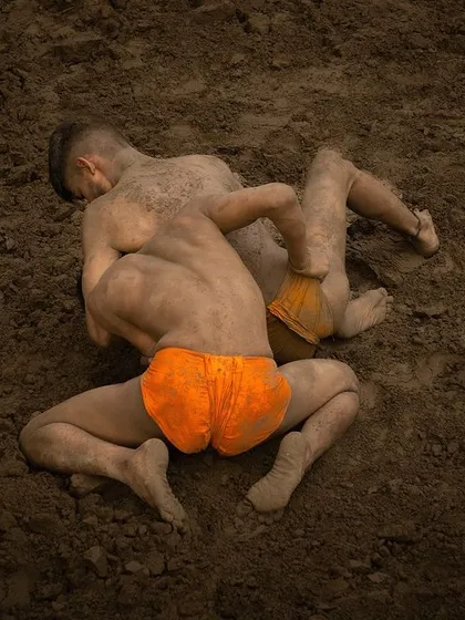 Two wrestlers, or 'pahalwan', grapple in a traditional mud pit. The photograph captures the raw strength and earthy texture of the indigenous sport of Kushti.
