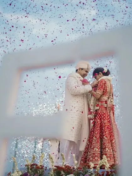 A creative shot of the varmala through the venue's architecture, framing the couple as they exchange garlands.