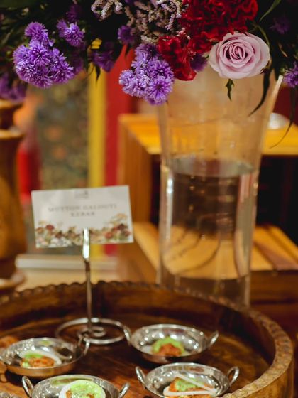 Mutton Galouti Kebabs served in small, individual silver bowls, garnished and ready to be served. The setup is enhanced with a beautiful floral arrangement in the background.