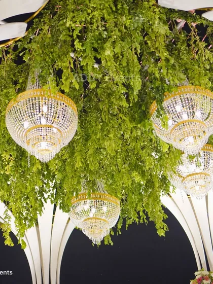A close-up of the details that create grandeur. Crystal chandeliers hang amidst a ceiling of fresh greenery, adding a touch of opulence and light to the wedding mandap.