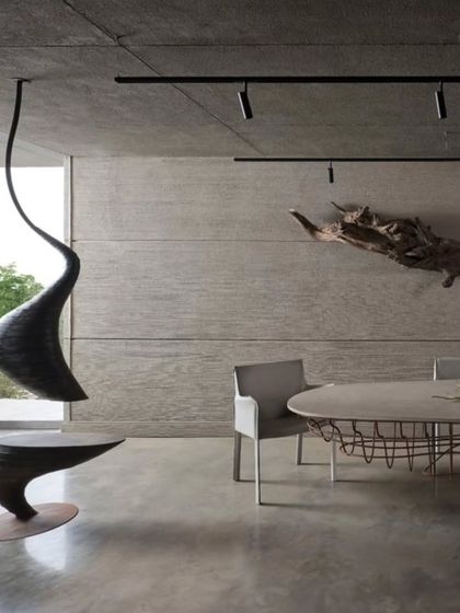 This meeting area features a sculptural hanging seat and a table with a delicate wireframe base, contrasting with the raw concrete walls and floor. A piece of driftwood mounted on the wall serves as natural art, reflecting my principle of finding beauty in raw, untouched materials.