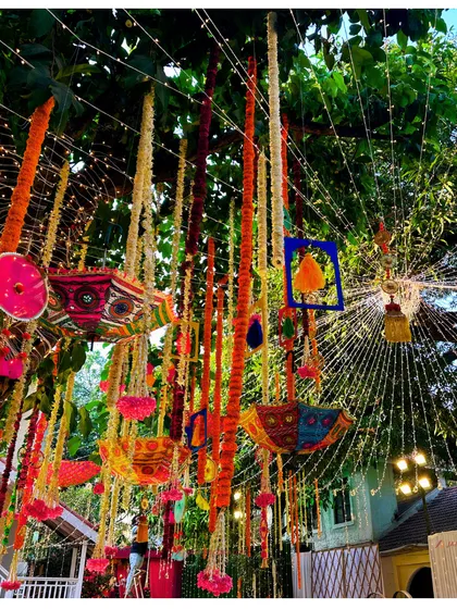 A whimsical ceiling of colorful umbrellas and floral tassels. This creative overhead decor adds a playful and festive touch to a Mehndi or Sangeet night.