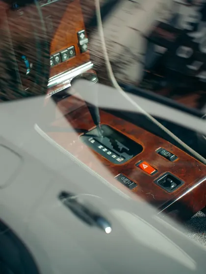 A detailed look at the wooden console and automatic gear shift of a classic car, seen through the window. These textures and materials tell a story of vintage luxury.