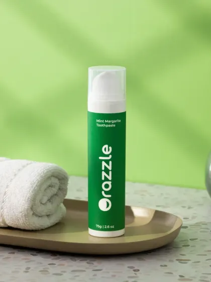 A minimalist lifestyle shot of a mint-flavored toothpaste in a bathroom setting. The clean composition, with a folded towel and a small plant, creates a fresh and modern aesthetic.