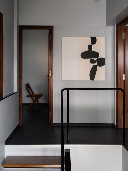 The upper-level landing in this duplex apartment acts as a gallery space for art. The simple black metal railing and dark flooring create a strong contrast with the white walls, guiding movement through the home.