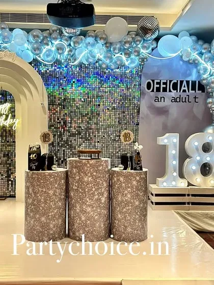 An elegant and modern setup for an 18th birthday party. This "Officially an Adult" theme features a silver sequin wall, a white arched backdrop, a neon "Happy Birthday" sign, and a chrome and silver balloon arch for a sophisticated celebration.