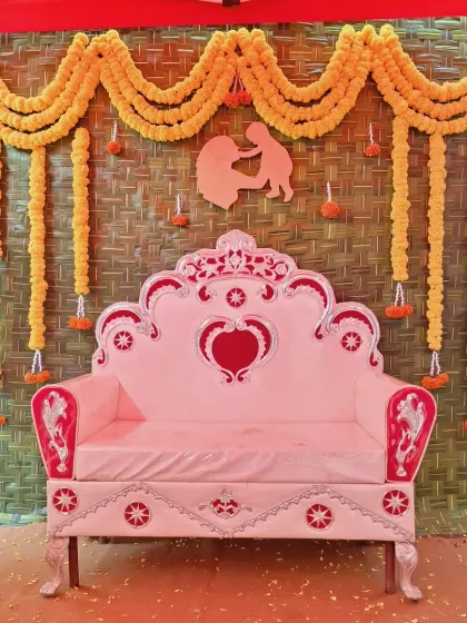 An outdoor baby shower decoration featuring a backdrop made from a woven mat, adorned with marigold garlands and a mother-child silhouette cutout.