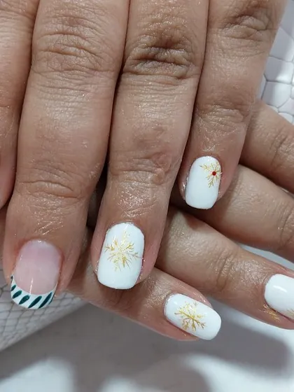 Get into the holiday spirit with this classy Christmas manicure. It features a crisp white base with hand-painted holly, gold snowflakes, and festive striped accent nails.